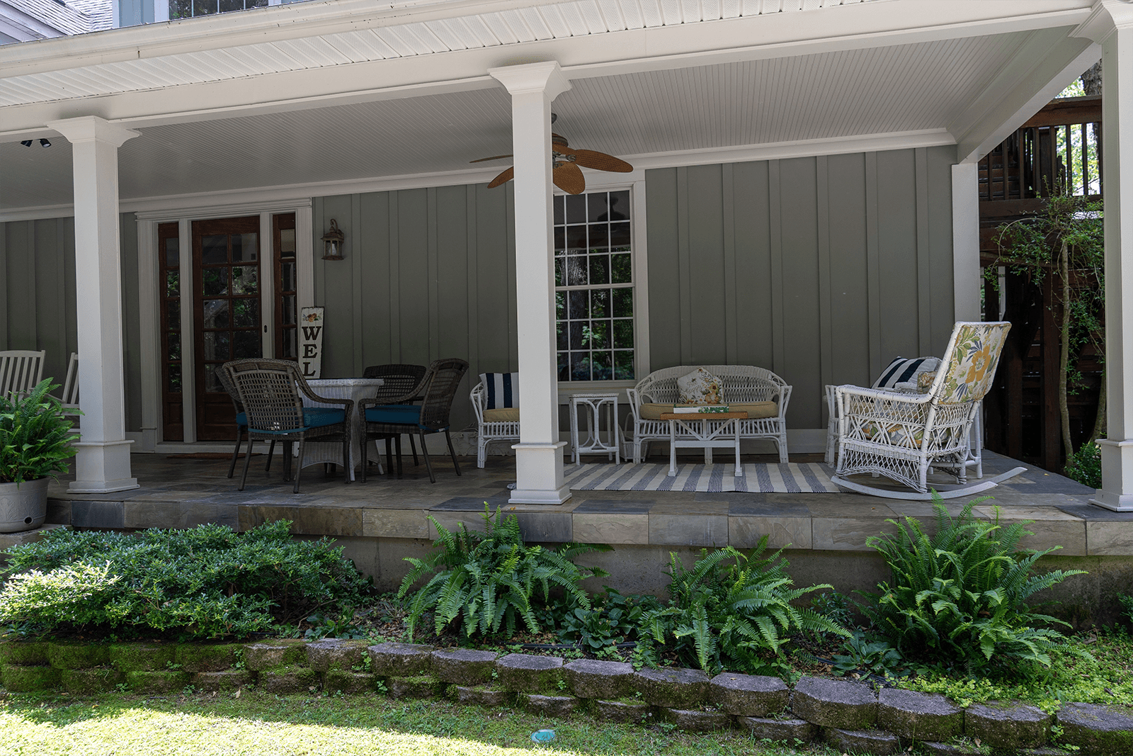 A cozy porch with wicker furniture, a dining table, and lush greenery.