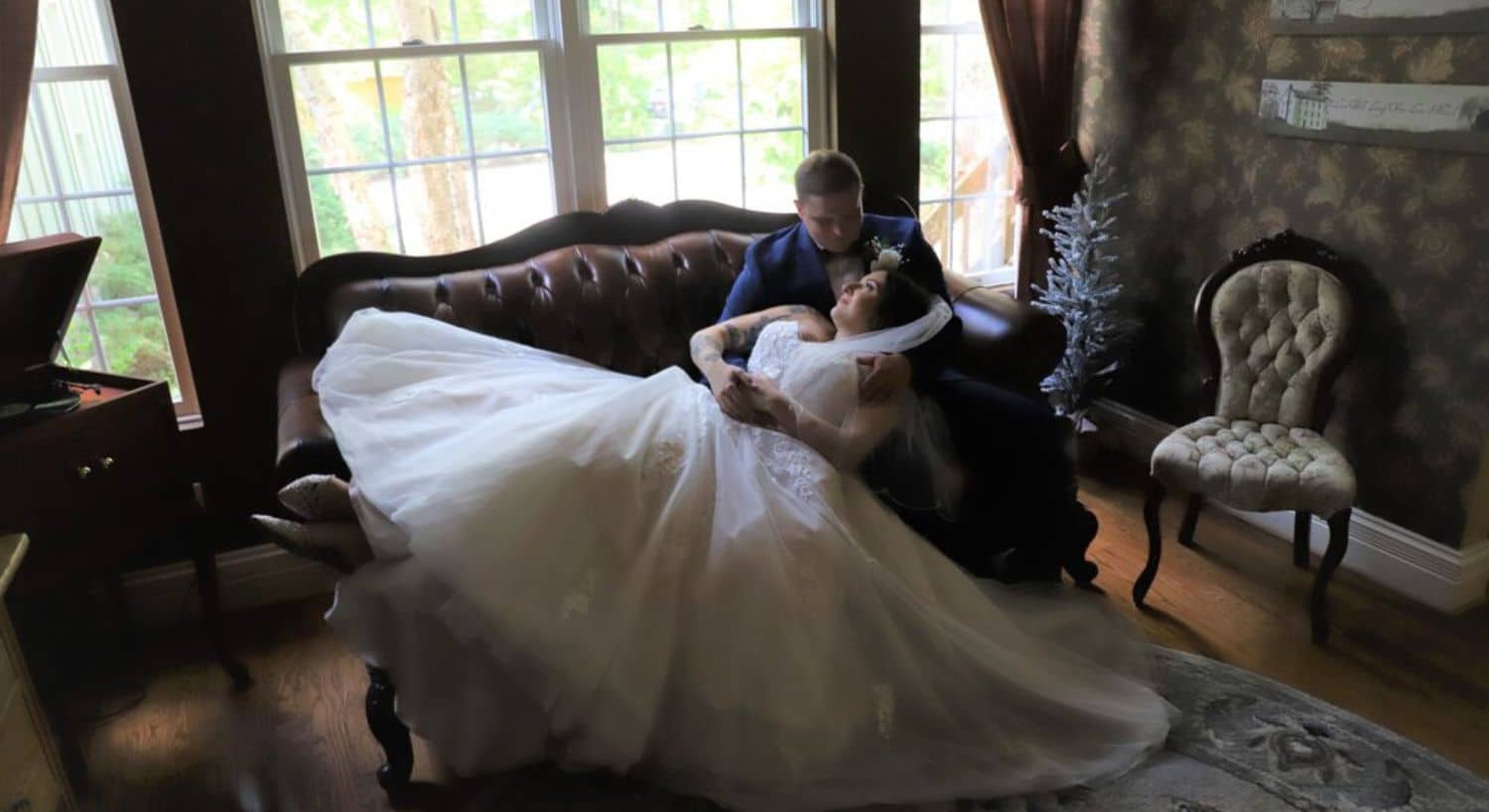 A couple embraces on a vintage sofa while the bride in a flowing white gown relaxes against the groom.