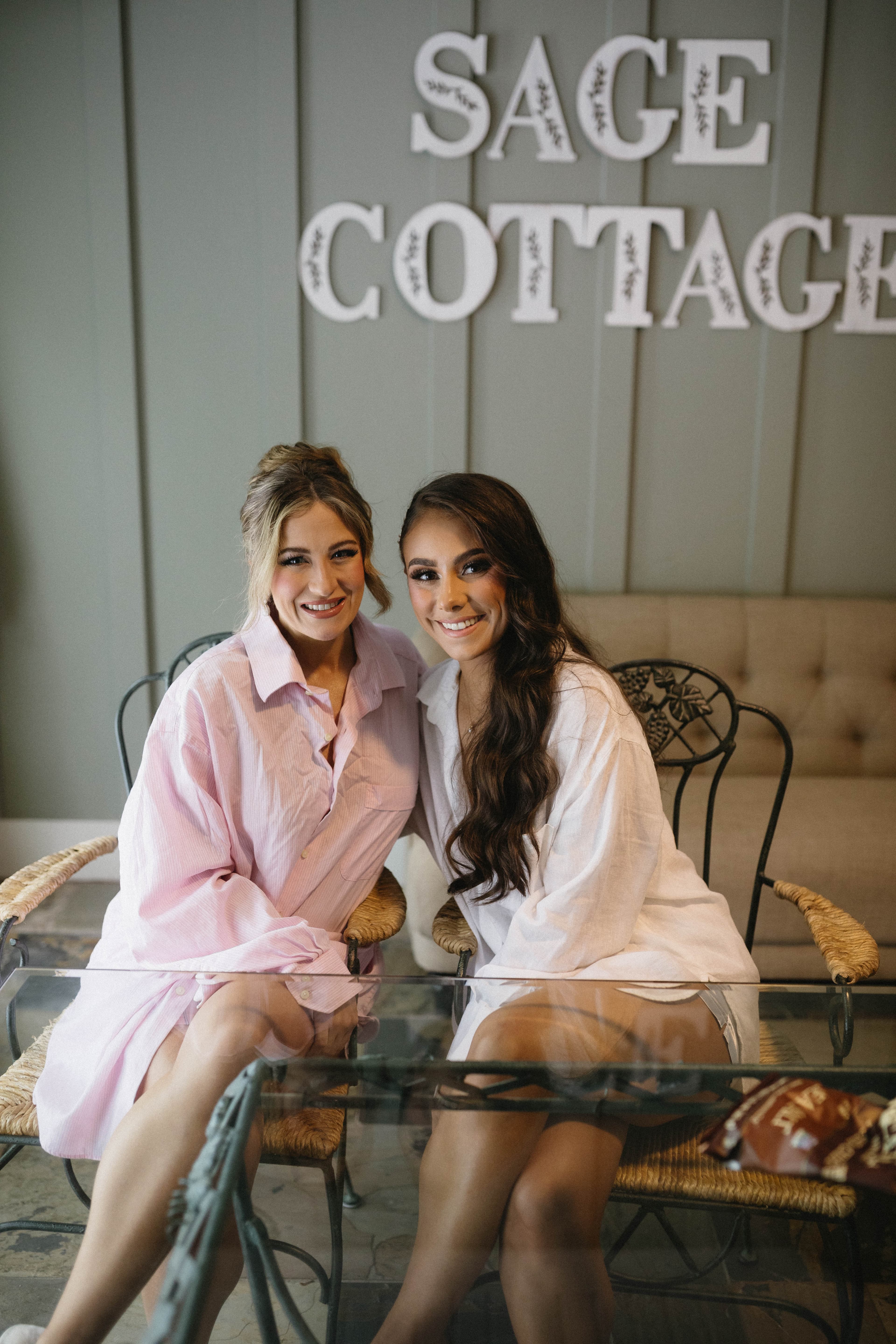 Two women smile warmly while seated together in a cozy setting, with "SAGE COTTAGE" displayed in the background.