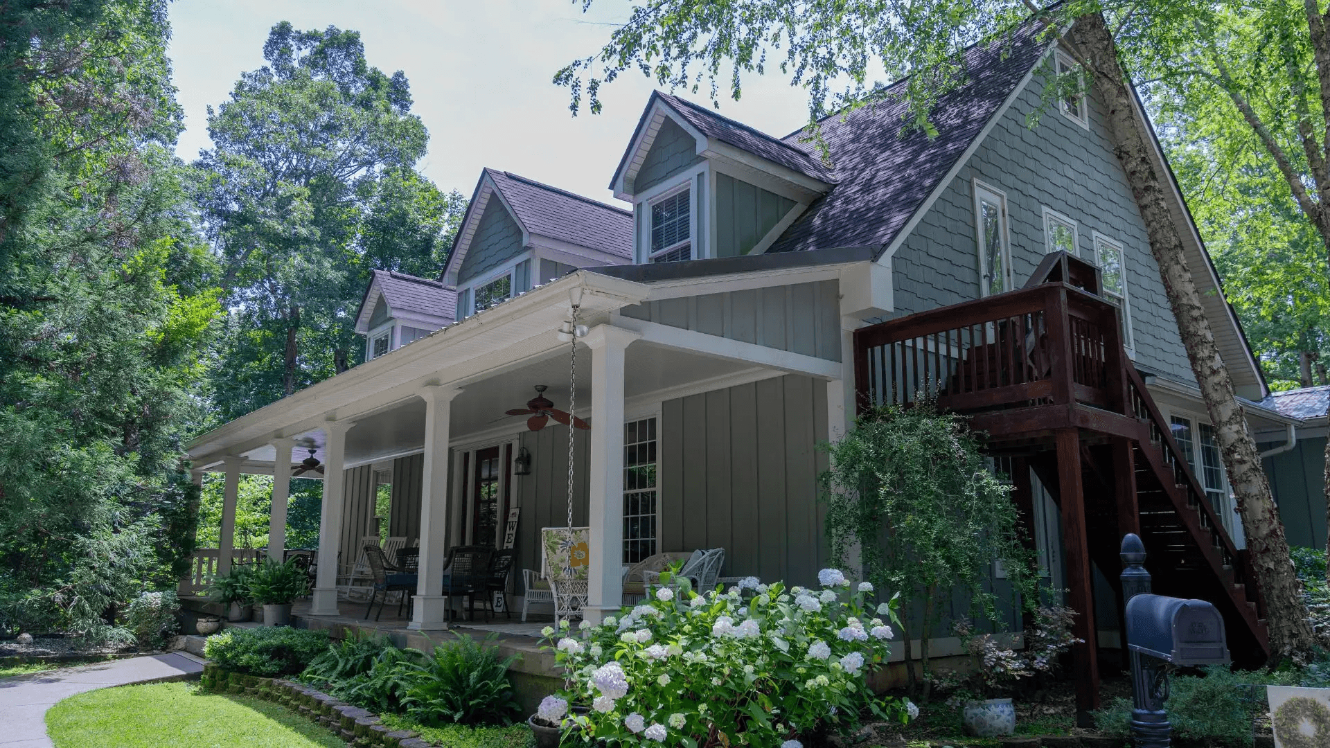 A charming two-story house with a porch and surrounded by greenery.