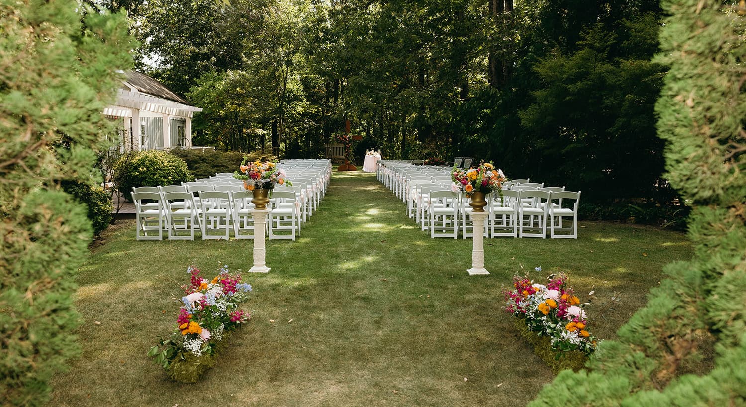 A serene outdoor wedding setup with rows of white chairs and colorful floral arrangements.