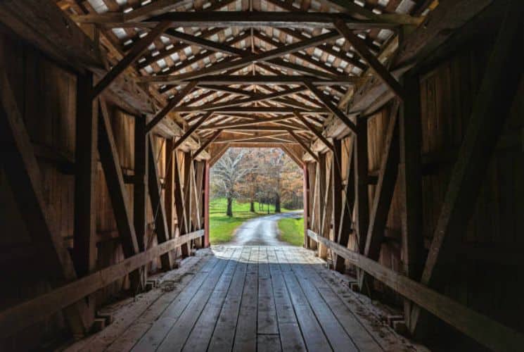 A covered bridge looking through to a tree lined road