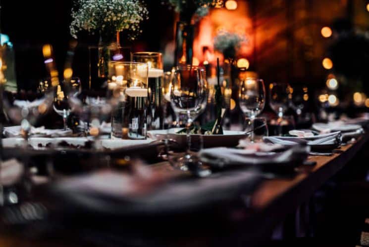 A restaurant table full of plates, napkins, water glasses, wine glasses and candles