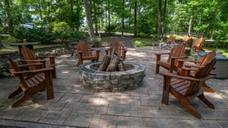 Outdoor brick patio with stone firepit surrounded by six wooden Adirondack chairs