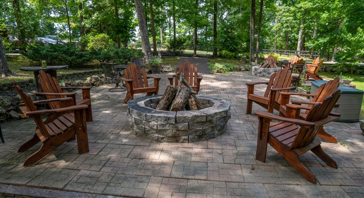 Outdoor brick patio with stone firepit surrounded by six wooden Adirondack chairs