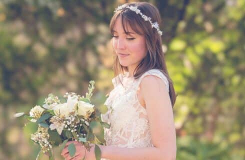 A bride in a lacy white dress and white flower wreath holding a bouquet of white flowers