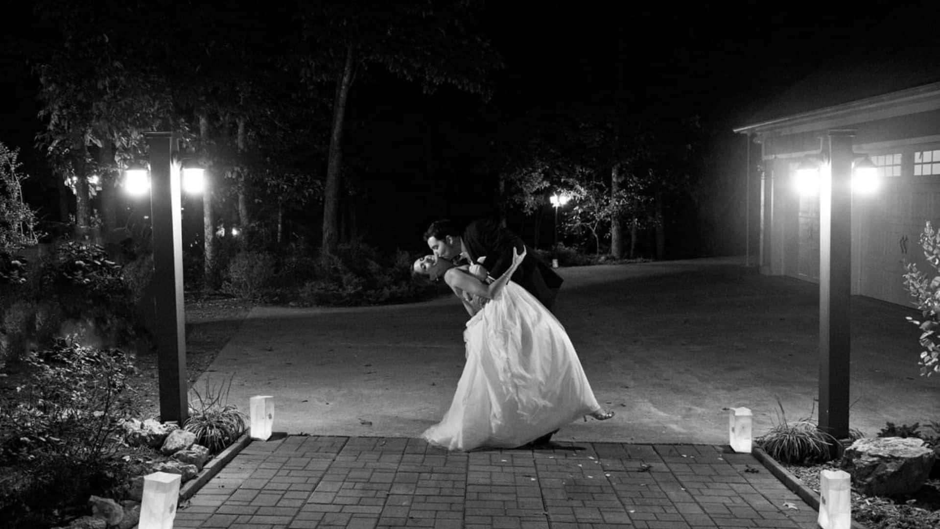 A groom dipping his bride on an outdoor brick patio with soft white lights and paper lanterns