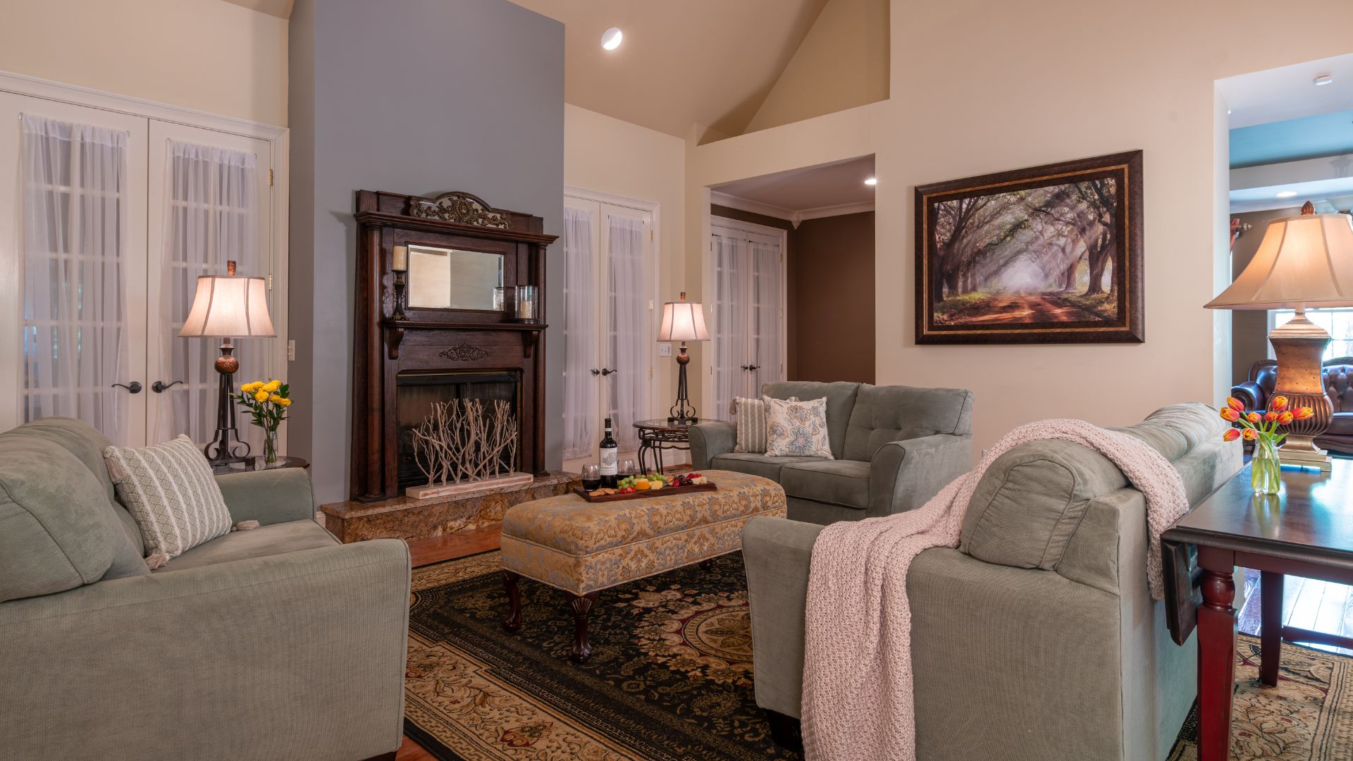 Elegant living room with grey couches and chair, ottoman, antique mantle with mirror and oriental rug