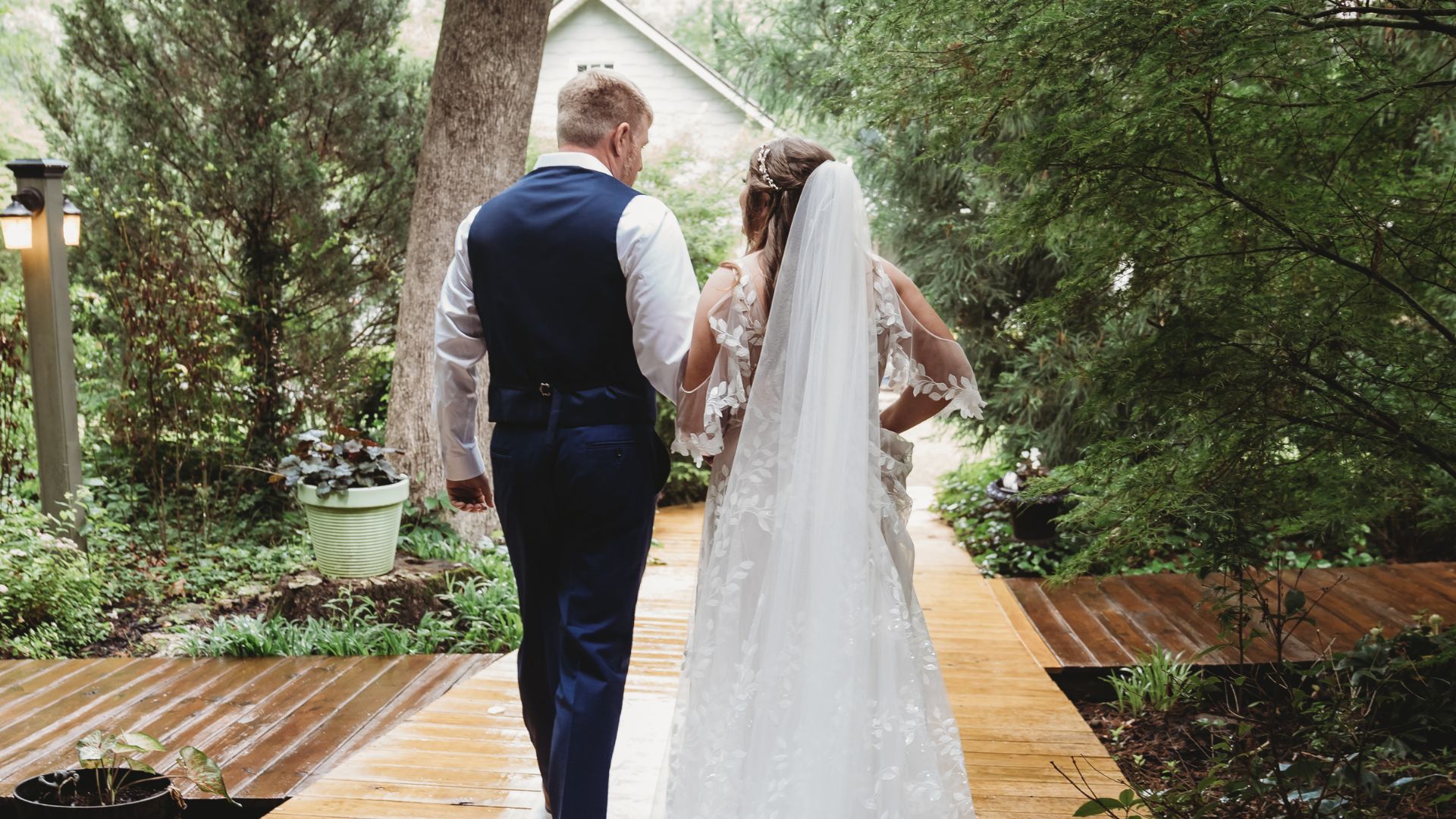 A bride and groom walking hand in hand on an wood path surrounded by trees