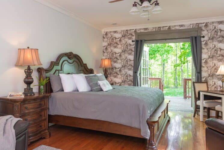 Elegant bedroom with bed, hardwood floors, decorative wallpaper, leather loveseat, table and two chairs and French doors to a patio