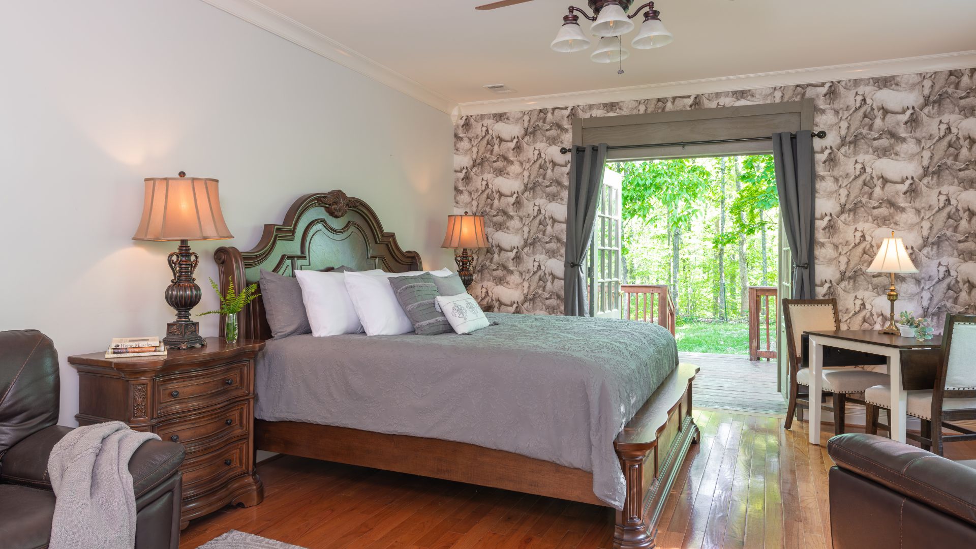 Elegant bedroom with bed, hardwood floors, decorative wallpaper, leather loveseat, table and two chairs and French doors to a patio