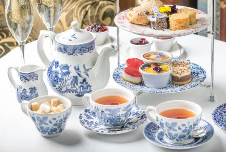 Blue and white tea set next to a two-tiered dessert tray full of small desserts