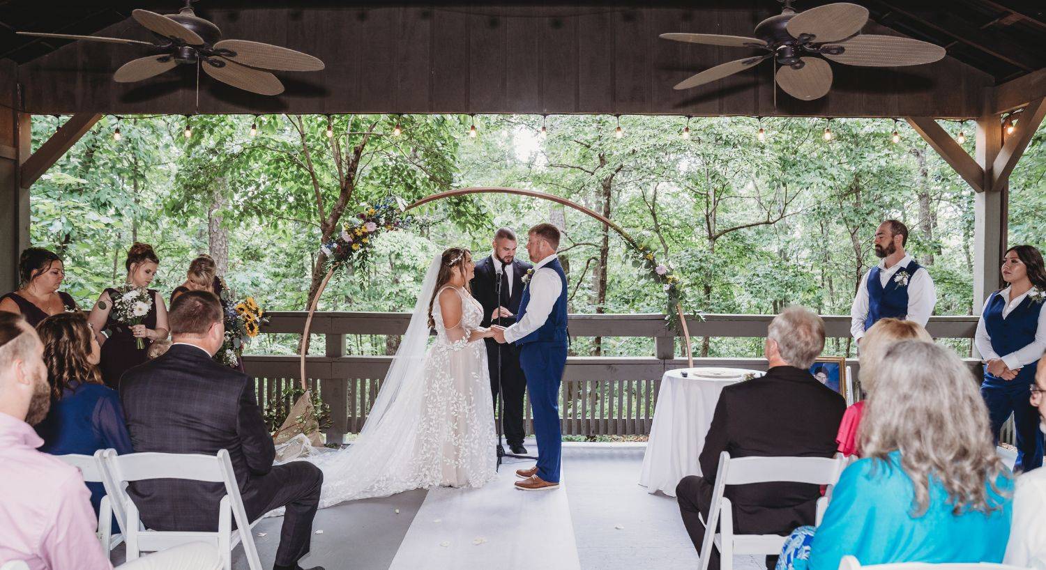 A bride and groom at an outdoor pavilion standing by a round arch wth flowers