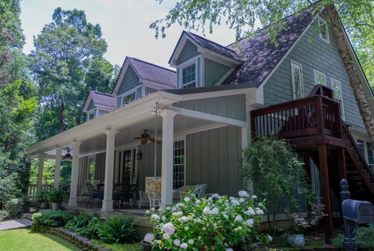 Exterior view of property painted gray with white trim and large front porch surrounded by bushes and large trees