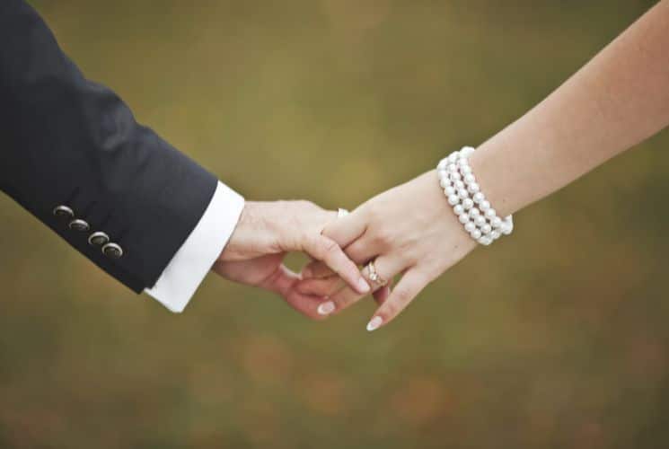 Arm with a suit jacket holding the hand of a woman with a pearl bracelet