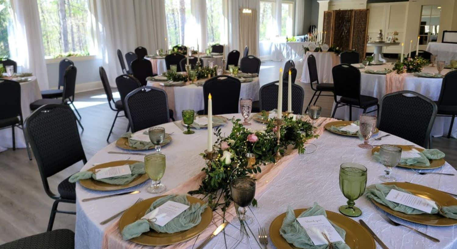 Event center with large windows and several round tables in white tablecloths and decorated for a wedding