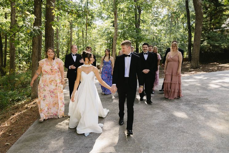 Bride and groom leading wedding party through the woods