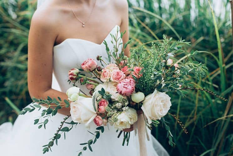 A bride in white holding a large bouquet of white and pink flowers