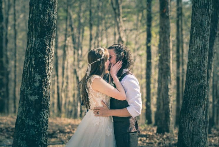 A bride and groom sharing a kiss in a forest with tall trees